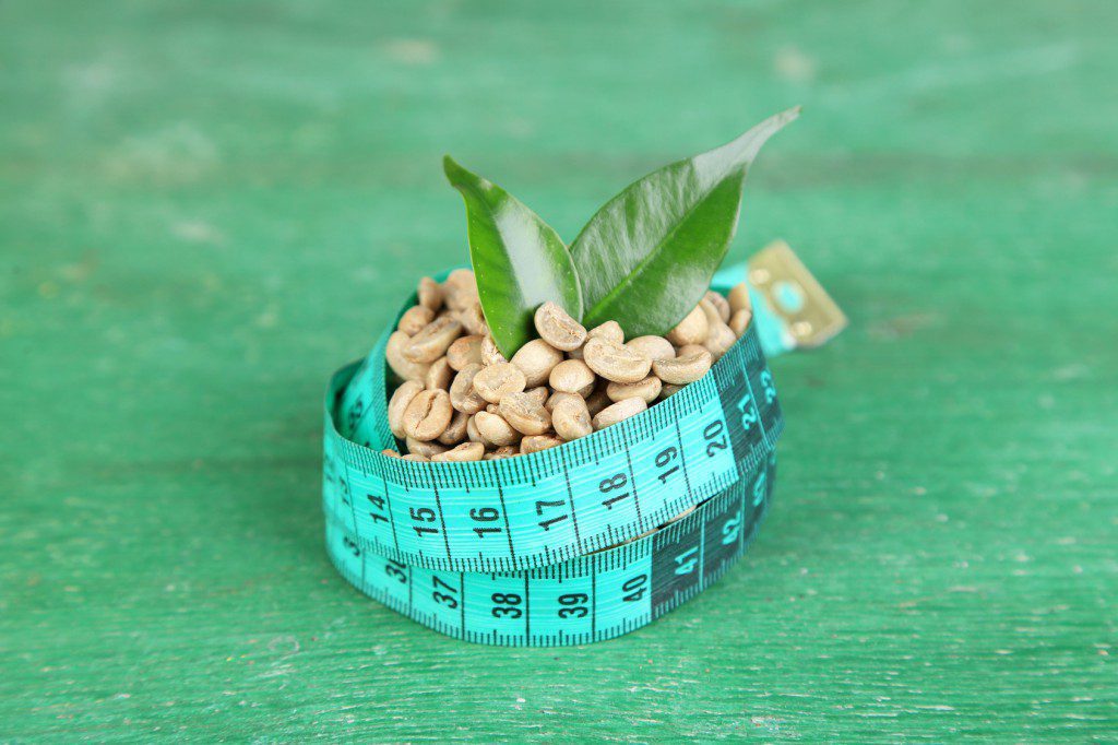 Raw green coffee beans and measuring tape, on color wooden background. Concept of weight loss